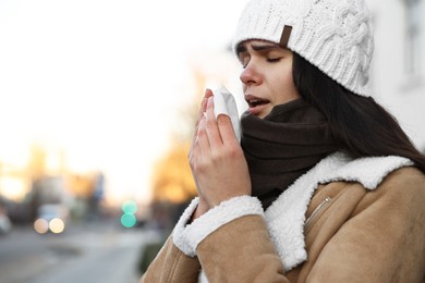 Photo of Woman with tissue blowing runny nose outdoors, space for text. Cold symptom