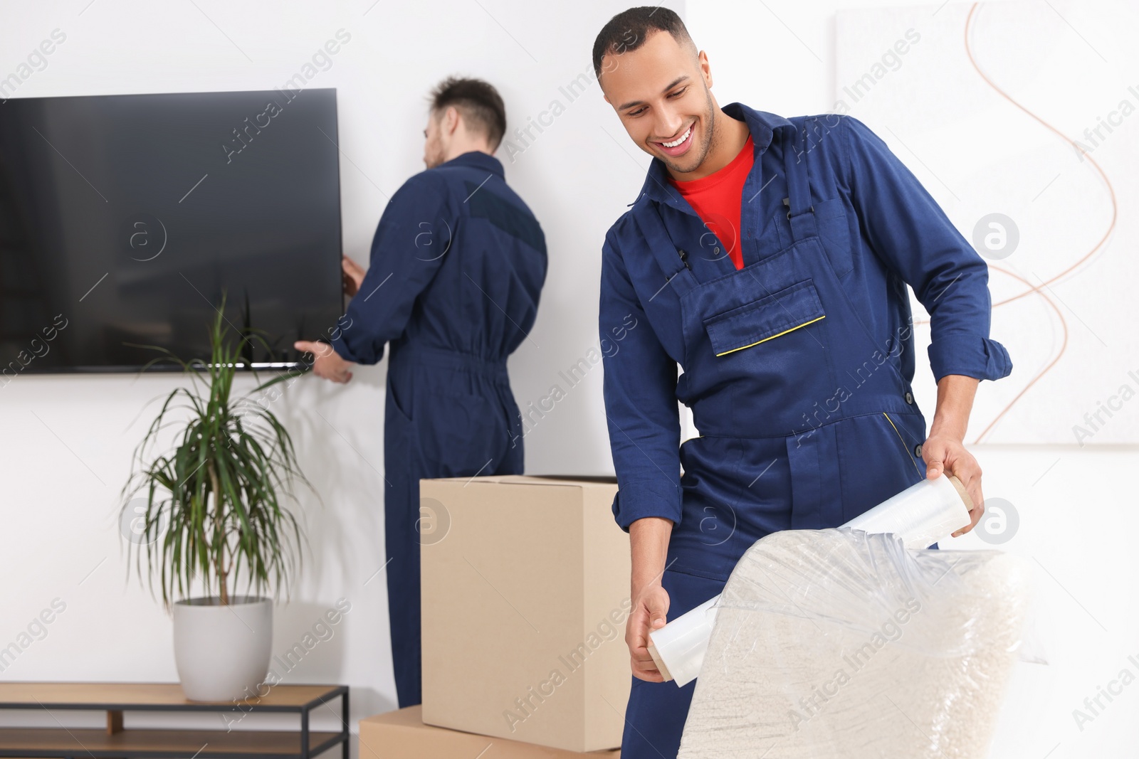 Photo of Male mover with stretch film wrapping armchair in house, space for text