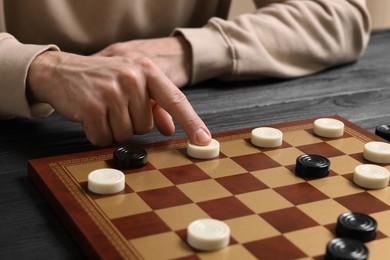 Photo of Playing checkers. Man thinking about next move at wooden table, closeup