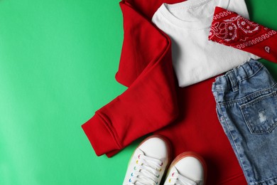 Stylish child clothes and shoes on green background, flat lay. Space for text