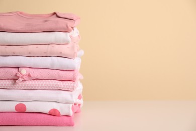 Stack of baby girl's clothes on white table. Space for text