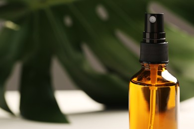Spray bottle of oil and green leaf on white table, closeup with space for text. Natural cosmetics