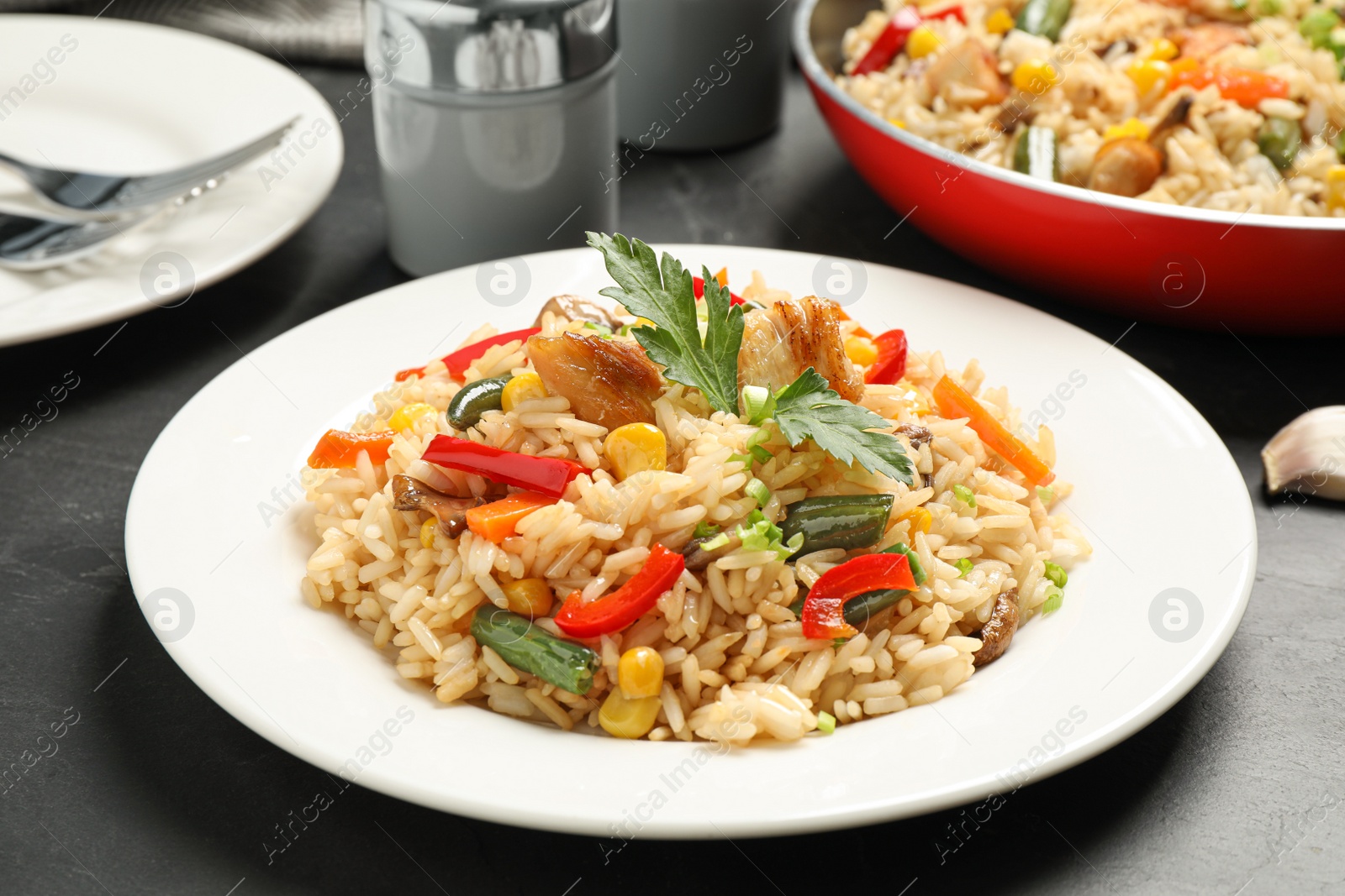 Photo of Delicious rice pilaf with chicken and vegetables on black table