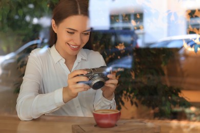 Photo of Young woman taking photocup with coffee at cafe, view through window. Creative hobby