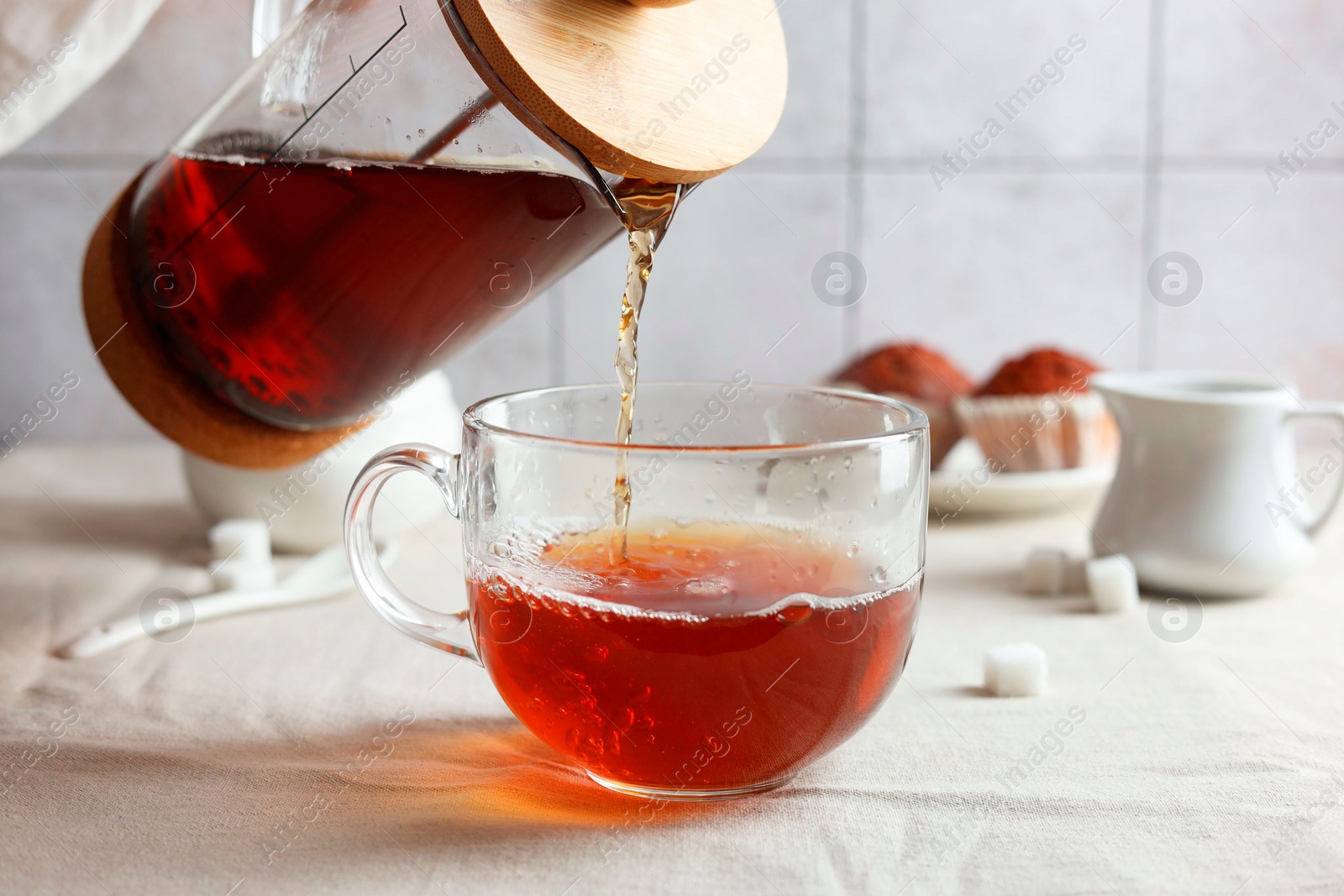 Photo of Pouring warm tea into cup on light table, closeup