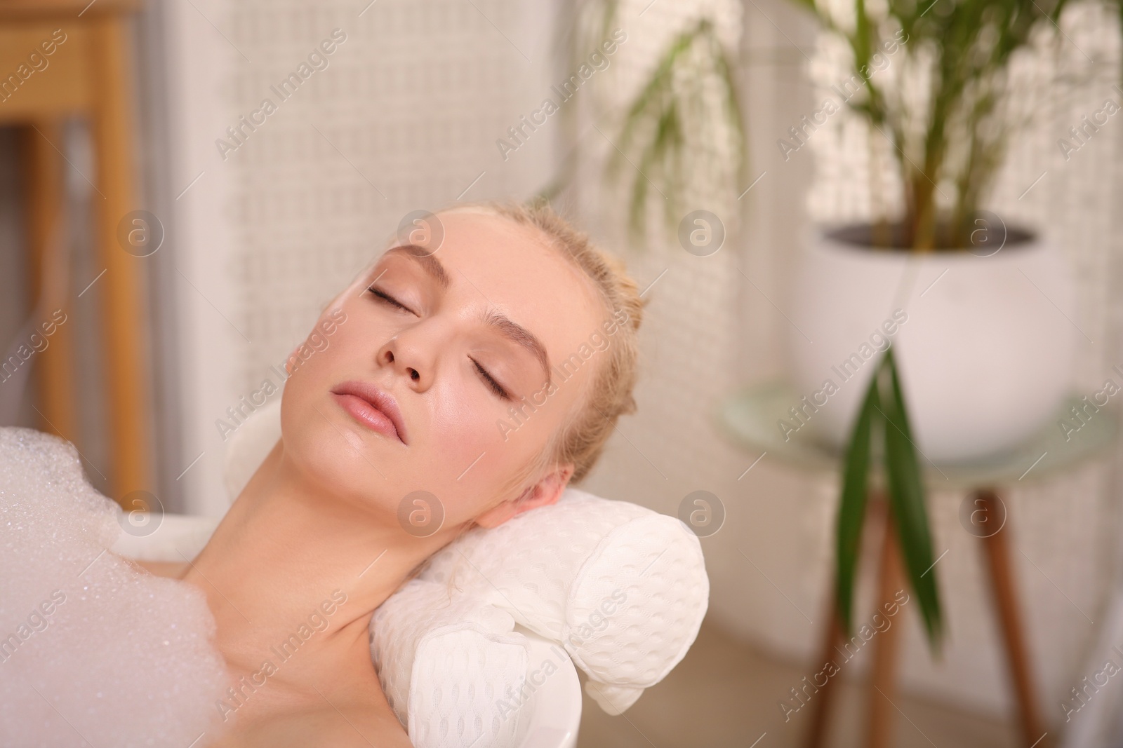 Photo of Young woman using pillow while enjoying bubble bath indoors