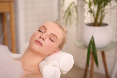 Young woman using pillow while enjoying bubble bath indoors