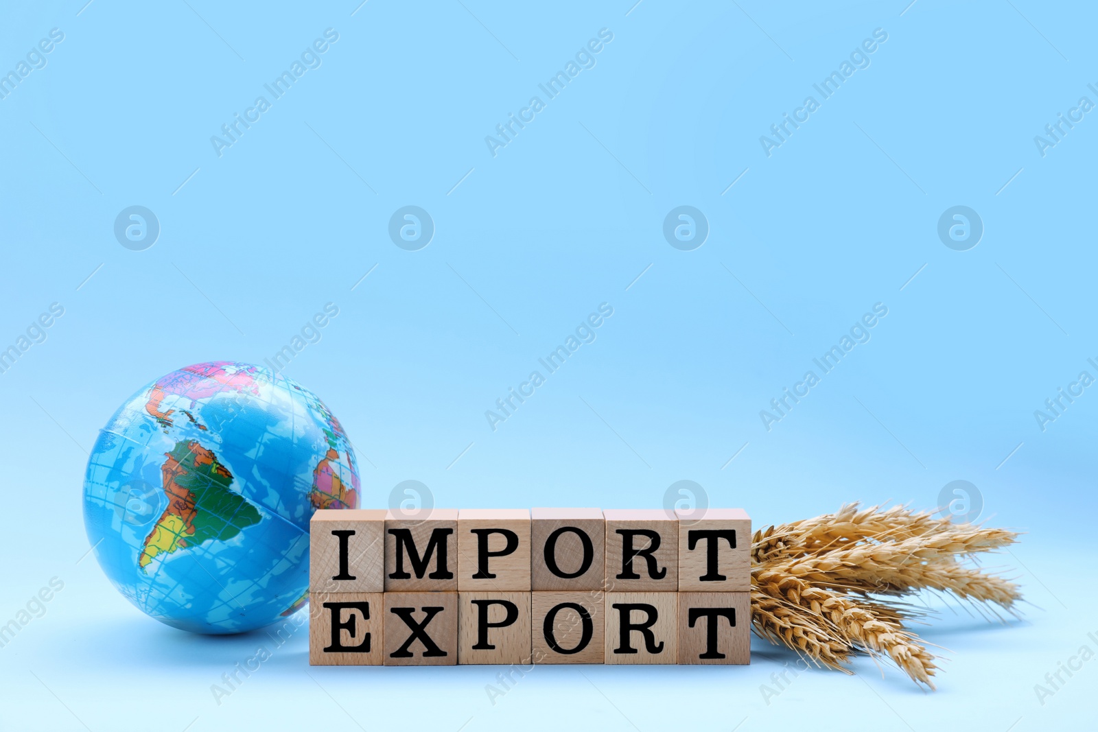 Photo of Words Import and Export made of wooden cubes, globe and ears of wheat on light blue background