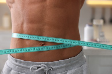 Photo of Athletic man measuring his waist with tape indoors, closeup. Weight loss