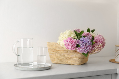 Photo of Beautiful hydrangea flowers in basket and water on light table