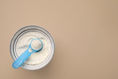 Photo of Top view of powdered infant formula with scoop in can on beige background, space for text. Baby milk