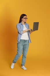 Photo of Young woman with modern laptop on yellow background