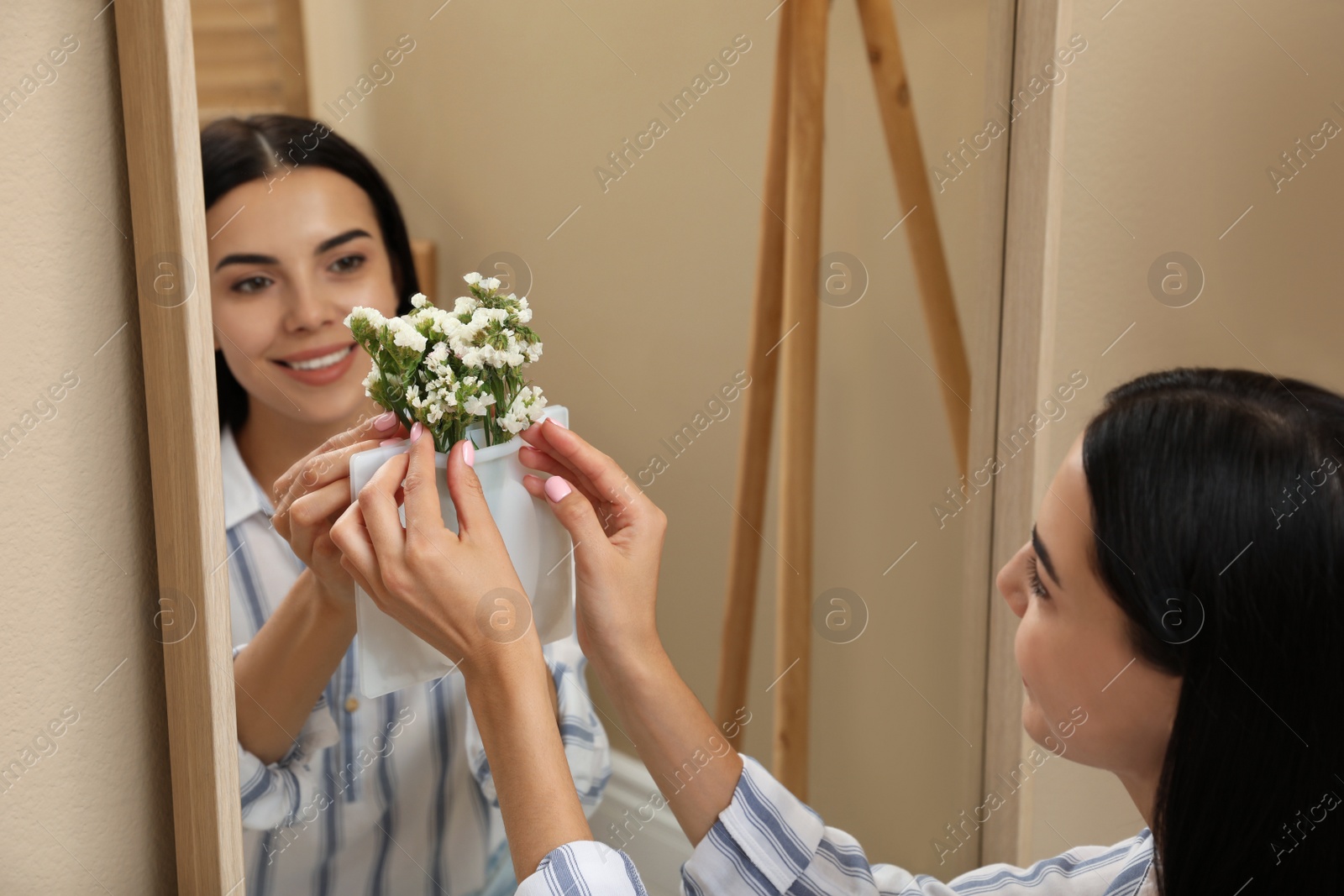 Photo of Happy woman putting flowers into silicone vase attached to mirror in room