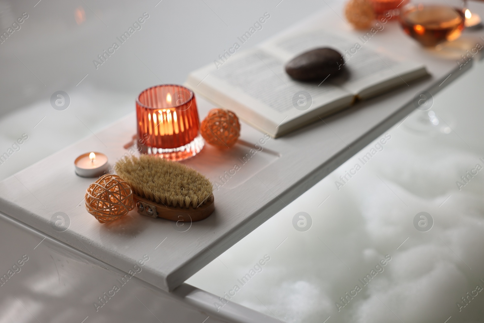 Photo of White wooden tray with burning candles and brush on bathtub