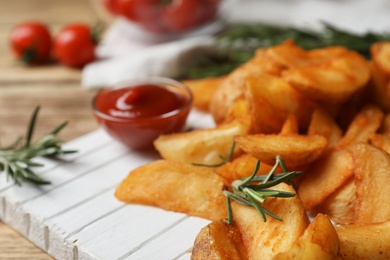 Photo of Wooden board with baked potatoes and rosemary on table, closeup