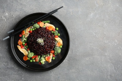 Photo of Plate with cooked brown rice and chopsticks on table, top view. Space for text