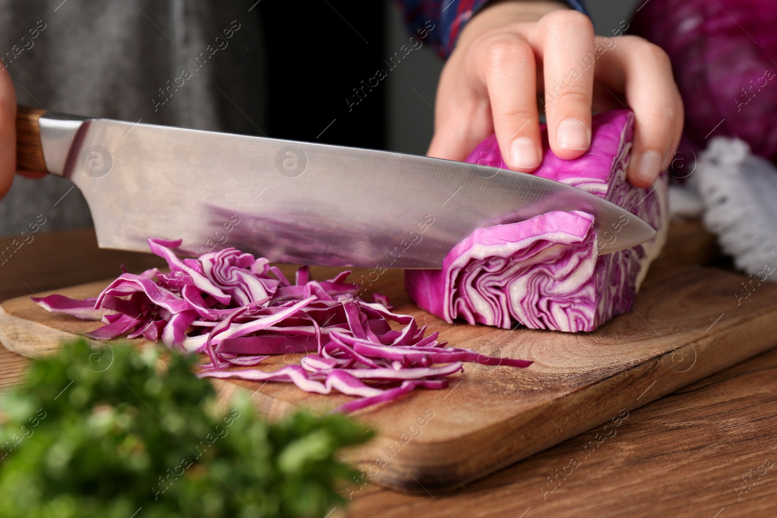 Photo of Woman cutting fresh red cabbage at wooden table, closeup