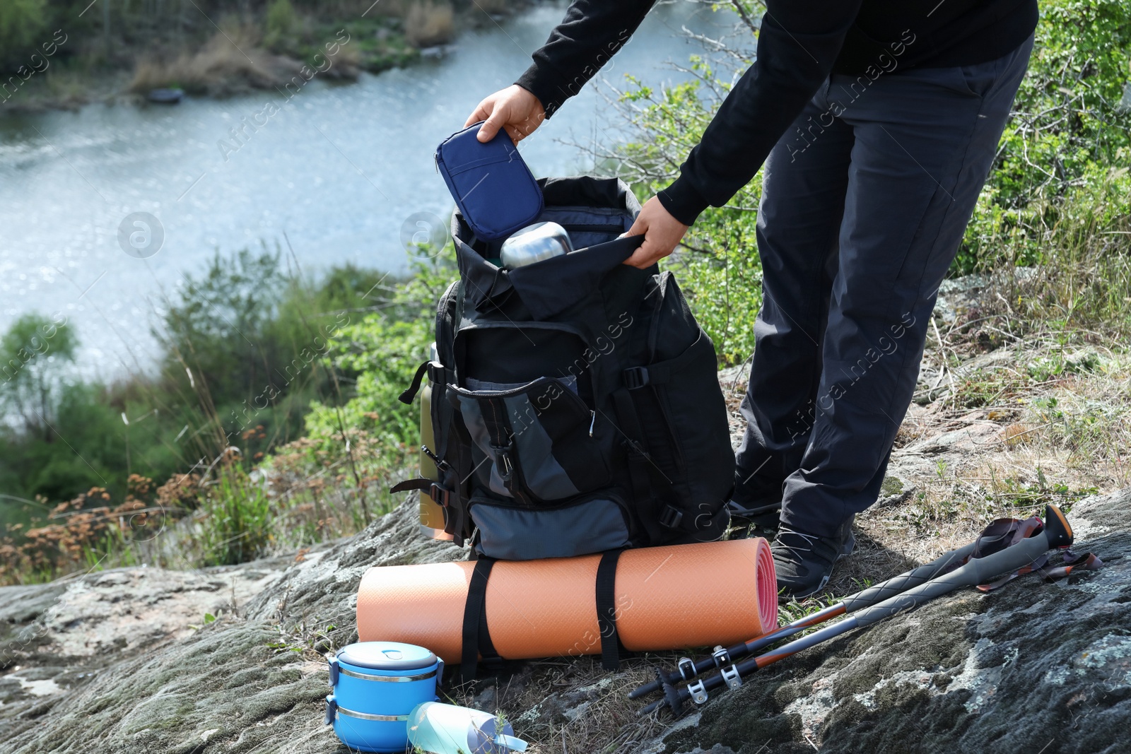 Photo of Hiker putting case into backpack on rocky hill near river, closeup