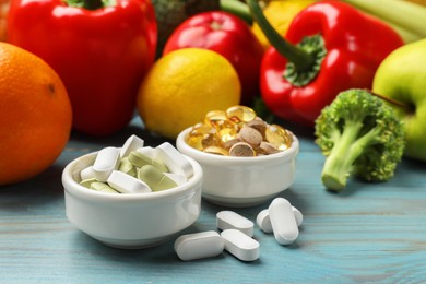 Photo of Dietary supplements. Bowls with different pills near food products on light blue wooden table, closeup