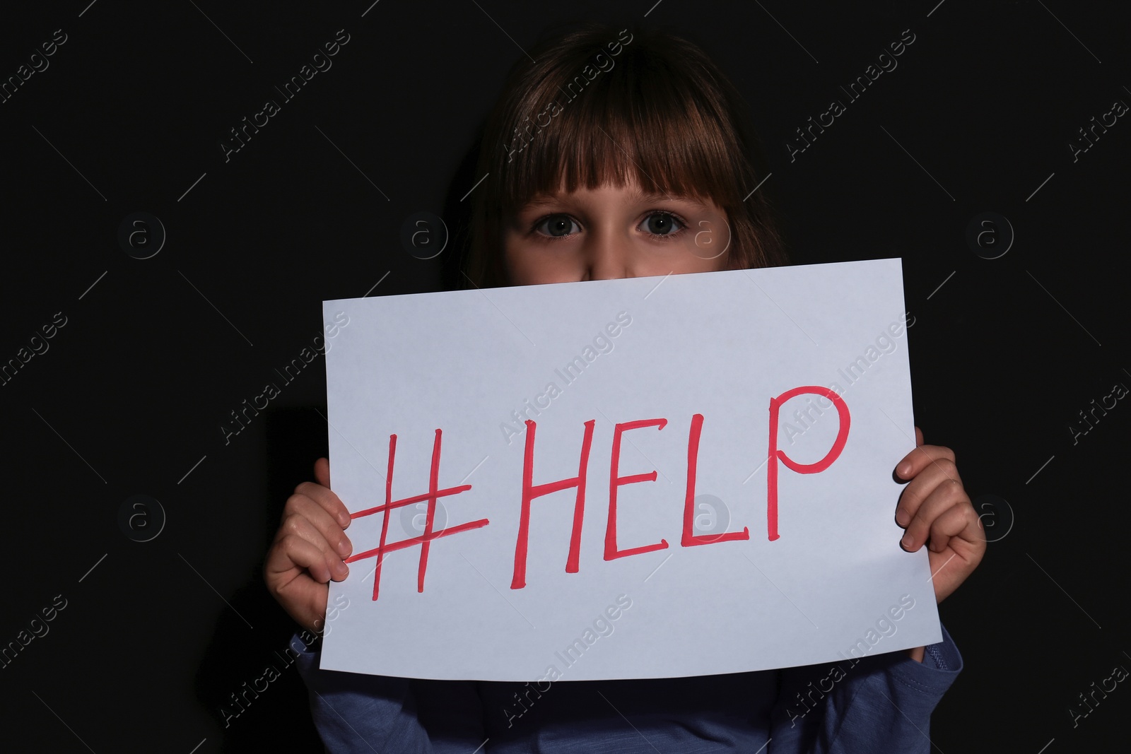 Photo of Abused little girl with hashtag HELP near black wall. Domestic violence concept