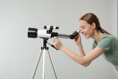 Photo of Young astronomer looking at stars through telescope on grey background