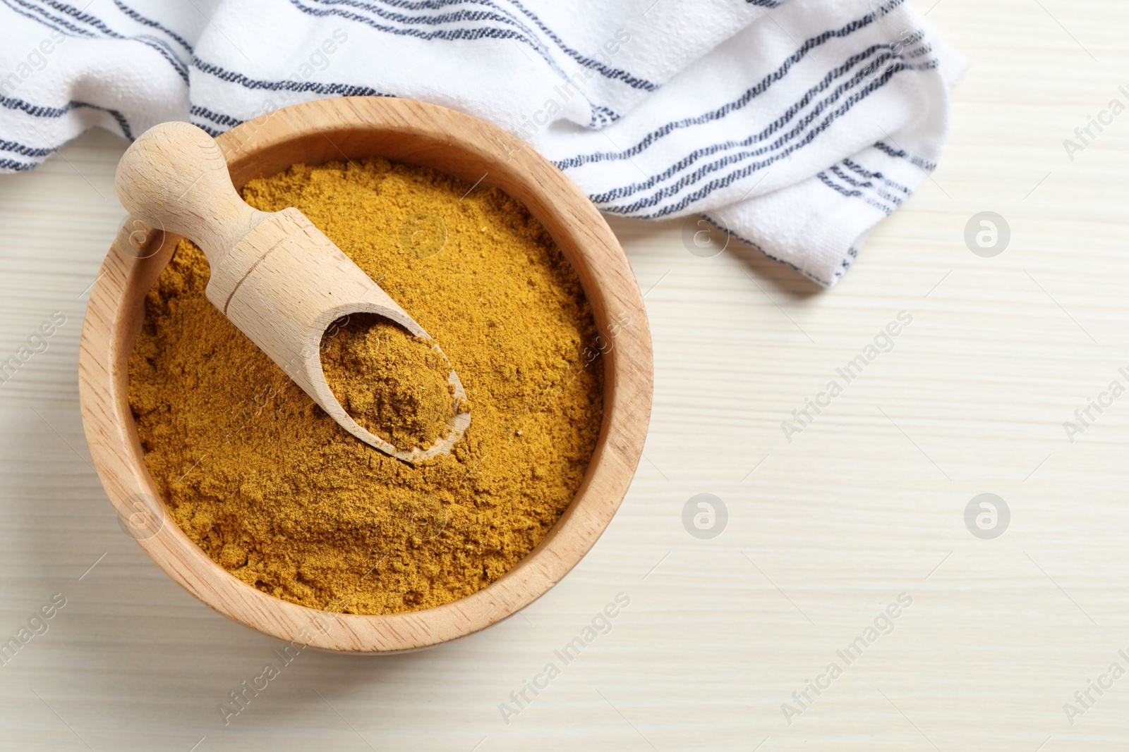 Photo of Dry curry powder in bowl and scoop on light wooden table, top view. Space for text