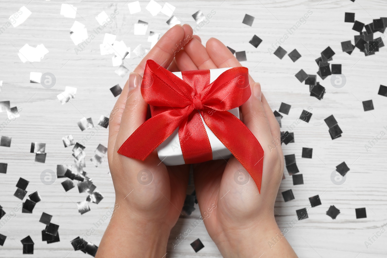 Photo of Christmas present. Woman with gift box and confetti on white wooden background, top view