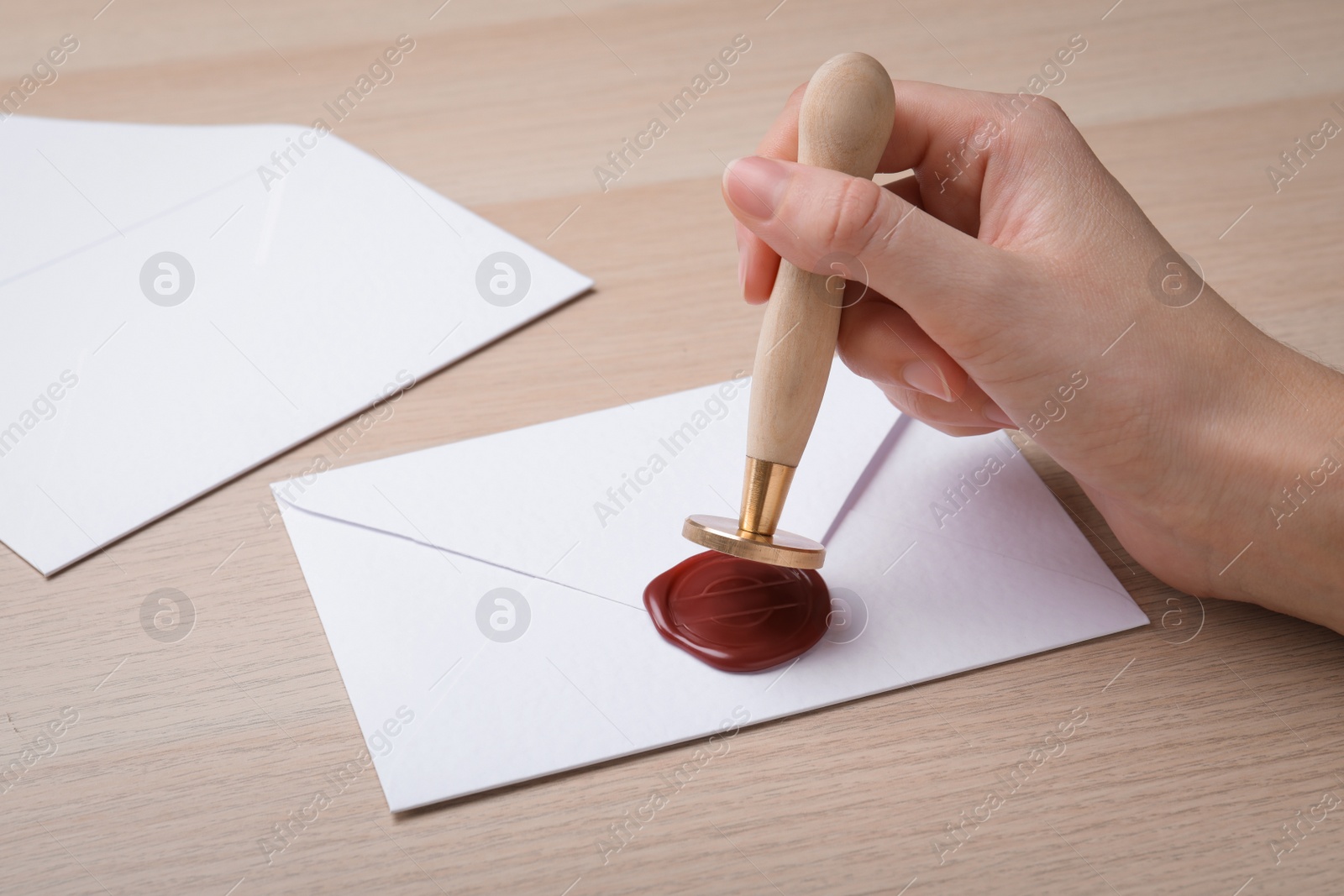 Photo of Woman sealing envelope at wooden table, closeup