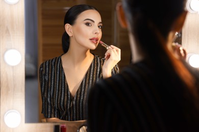 Photo of Bright makeup. Beautiful woman applying lipstick near mirror in dressing room