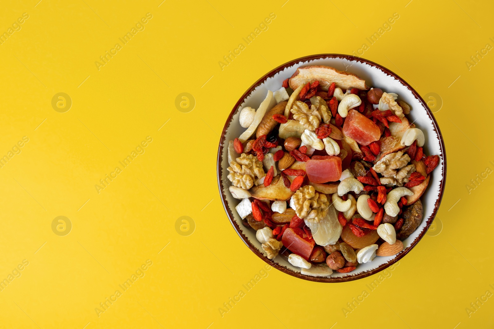 Photo of Bowl with mixed dried fruits and nuts on yellow background, top view. Space for text