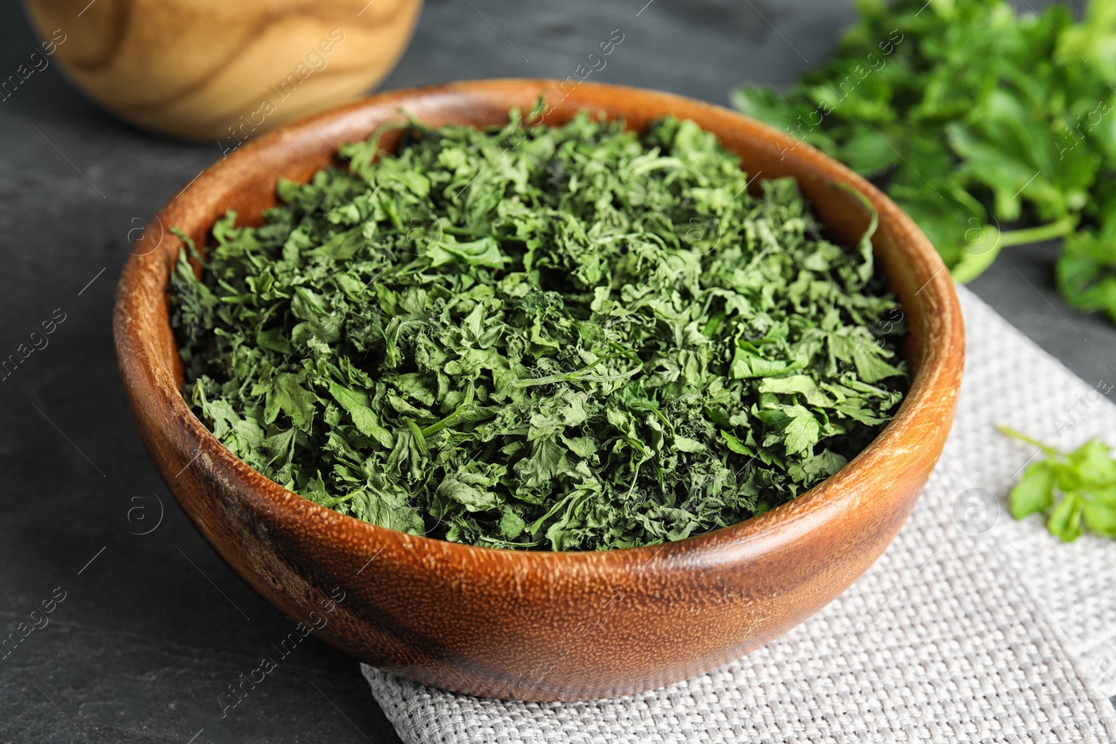 Photo of Wooden bowl of dried parsley on table, closeup