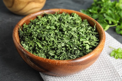 Photo of Wooden bowl of dried parsley on table, closeup