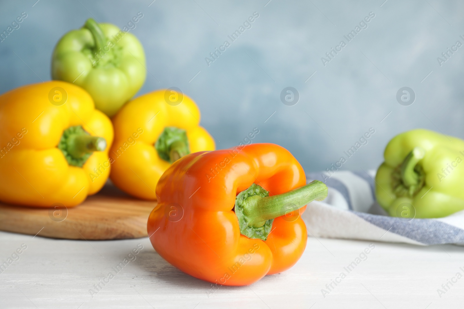 Photo of Fresh ripe bell peppers on wooden table against light blue background