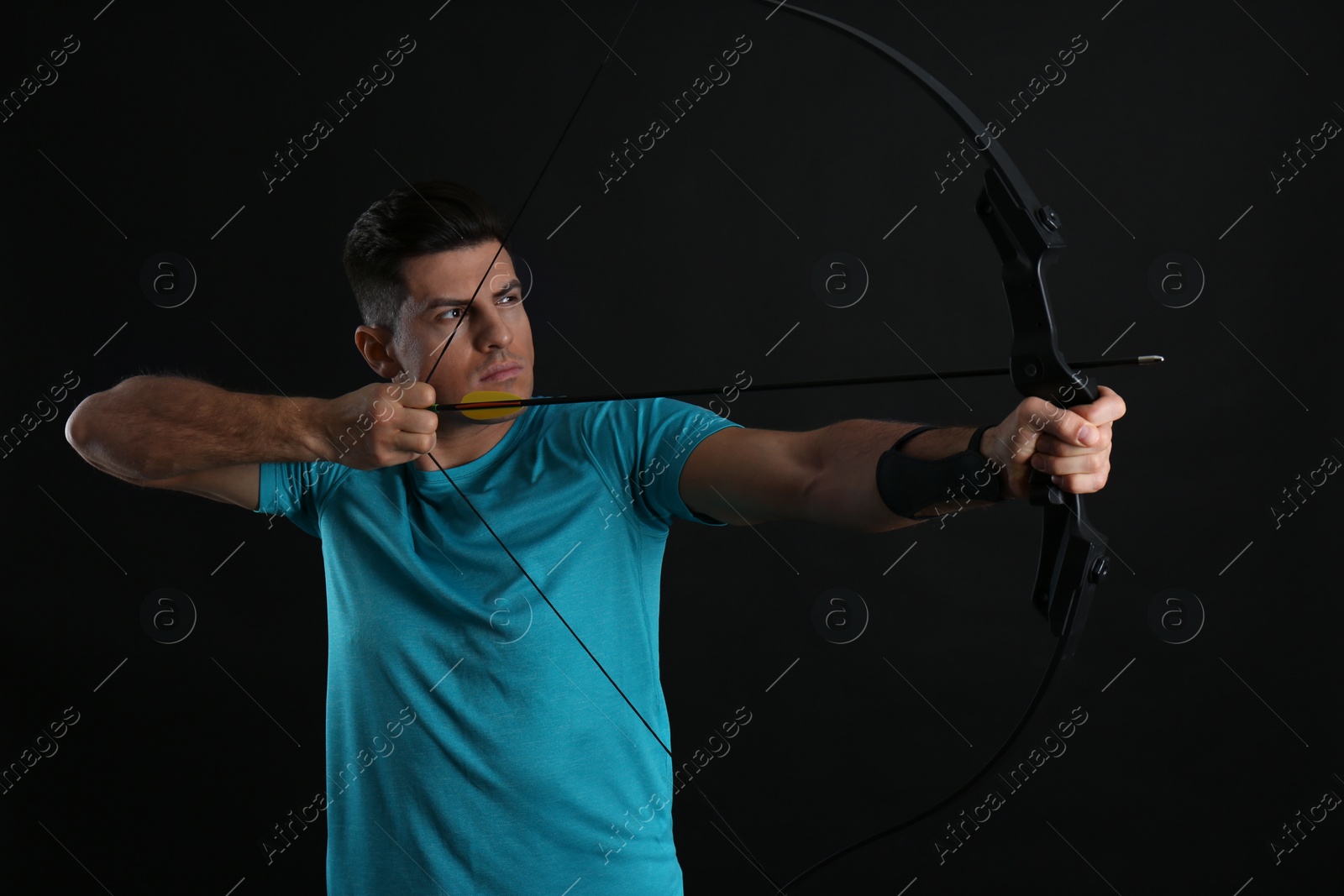 Photo of Man with bow and arrow practicing archery on black background