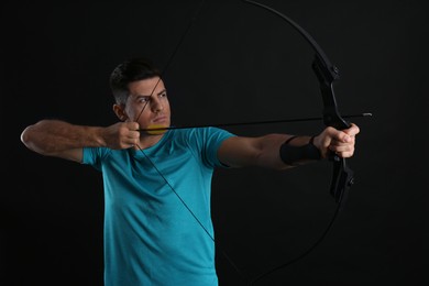Man with bow and arrow practicing archery on black background