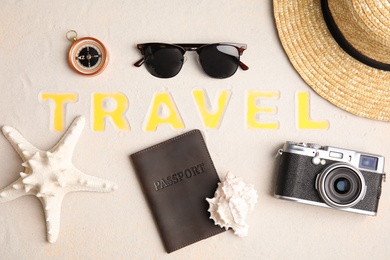 Flat lay composition with different tourist objects and word TRAVEL on sand