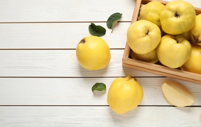 Photo of Fresh ripe organic quinces and leaves on white wooden table, flat lay. Space for text