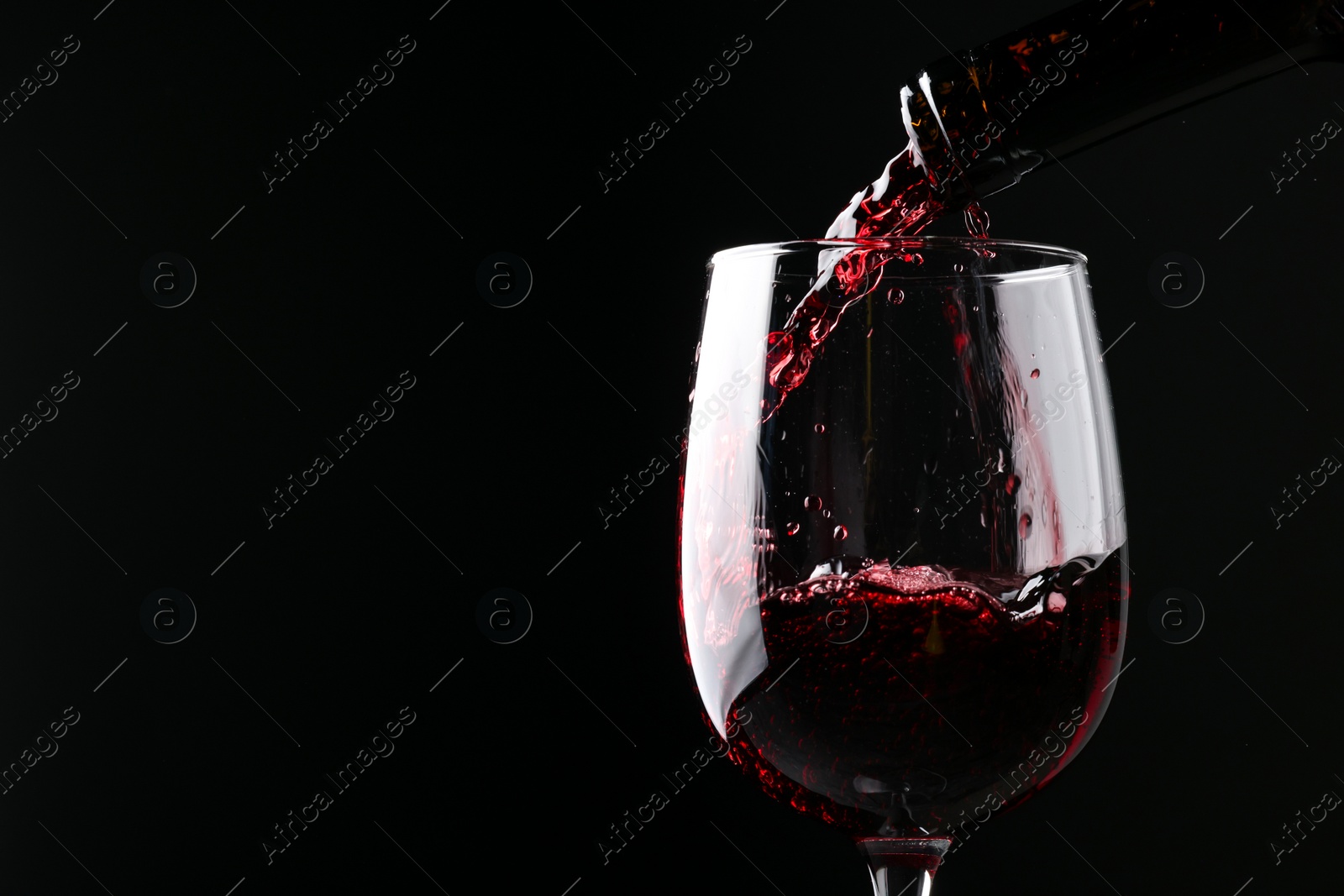 Photo of Pouring red wine into glass against black background, closeup. Space for text