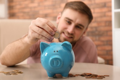 Photo of Young man with piggy bank and money at home, closeup