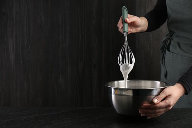 Photo of Woman making whipped cream with whisk at black table, closeup. Space for text