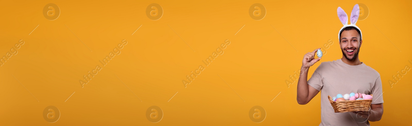 Image of Man with bunny ears holding basket full of Easter eggs on orange background, space for text. Banner design