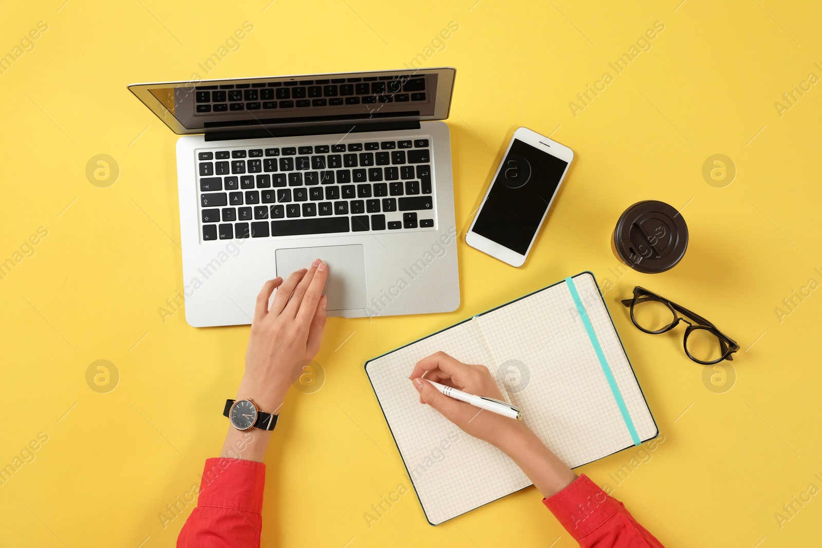 Photo of Woman working with modern laptop and writing in notebook at color table, top view