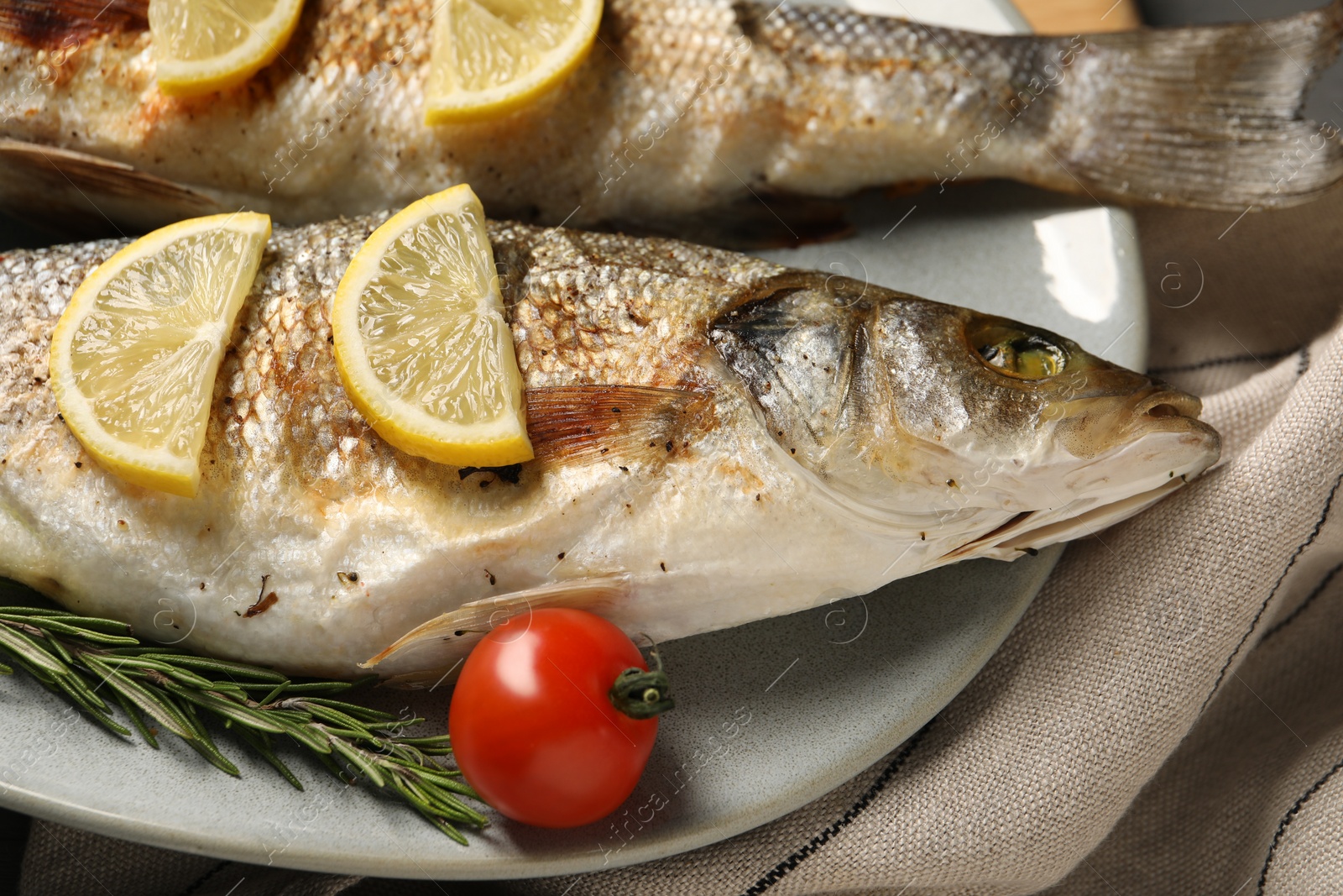 Photo of Delicious baked fish, tomato, lemon and rosemary on table, closeup