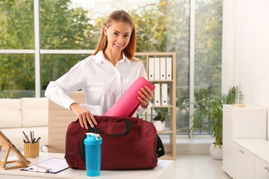 Photo of Businesswoman packing sports stuff for training into bag in office