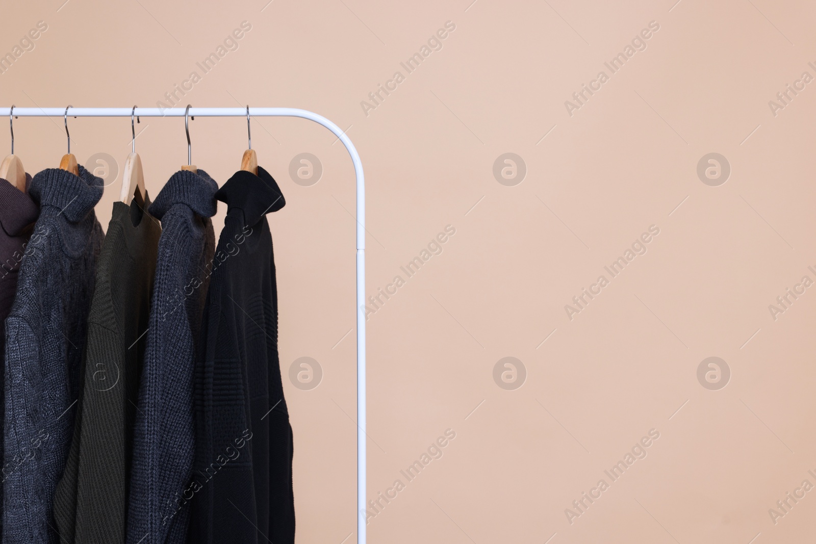Photo of Rack with different warm sweaters on beige background. Space for text