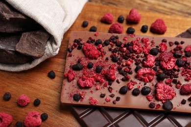 Photo of Different chocolate bars with freeze dried fruits on wooden board, closeup