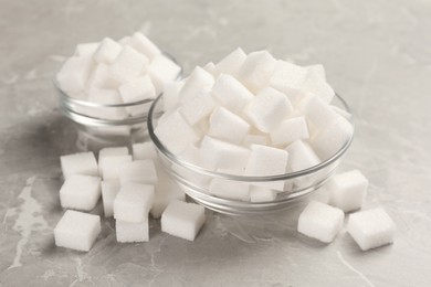 Photo of Bowls with sugar cubes on grey marble table, closeup