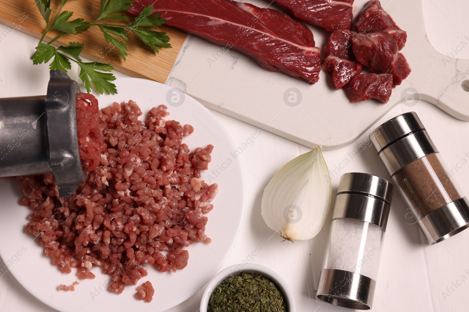 Photo of Manual meat grinder with beef, onion and spices on white table, flat lay