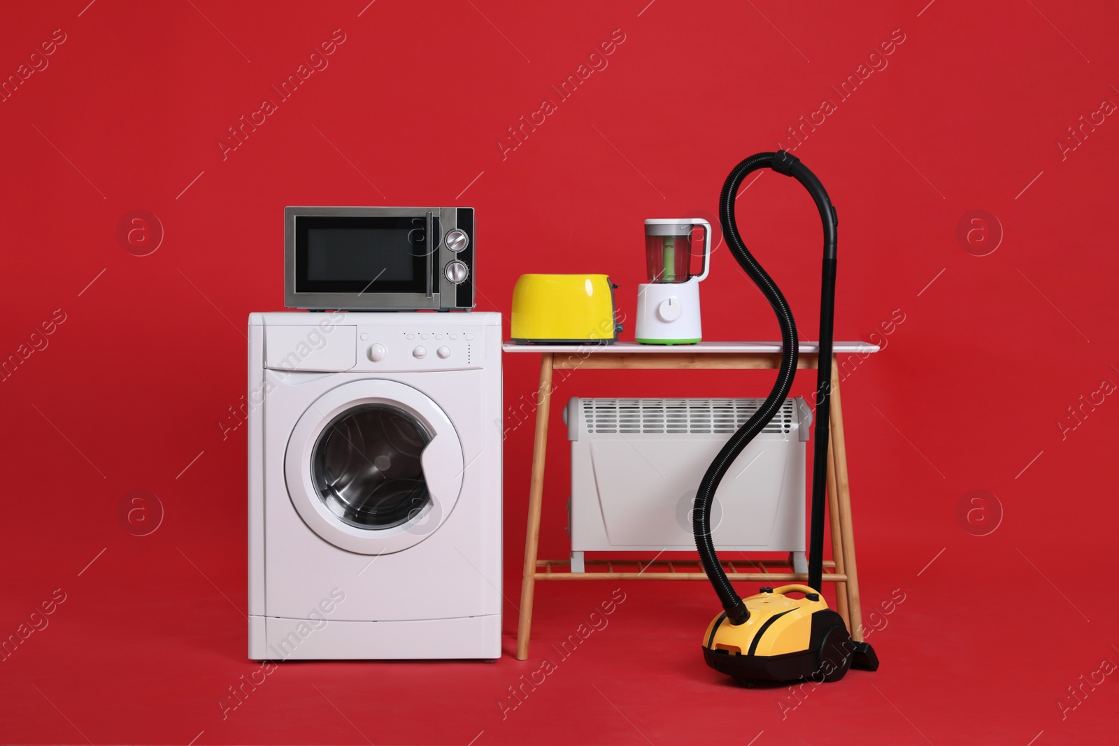 Photo of Set of different home appliances with vacuum cleaner on red background