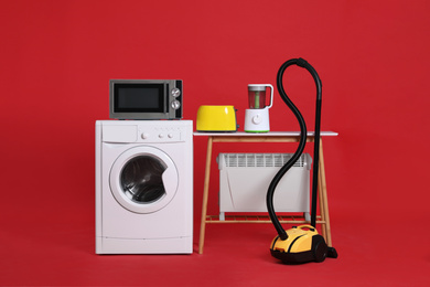 Photo of Set of different home appliances with vacuum cleaner on red background